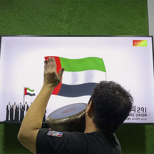 Guest playing Drum-to-Reveal interactive game at a Dubai event, beating the drum to reveal a hidden image on a large screen, designed for exhibitions and activations.