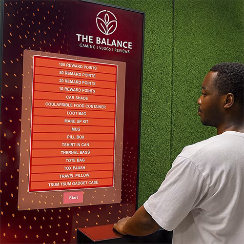 Guest playing interactive event game at exhibition booth in Dubai, pressing button to win prize, with branded screen display and selfie sharing feature for engagement.