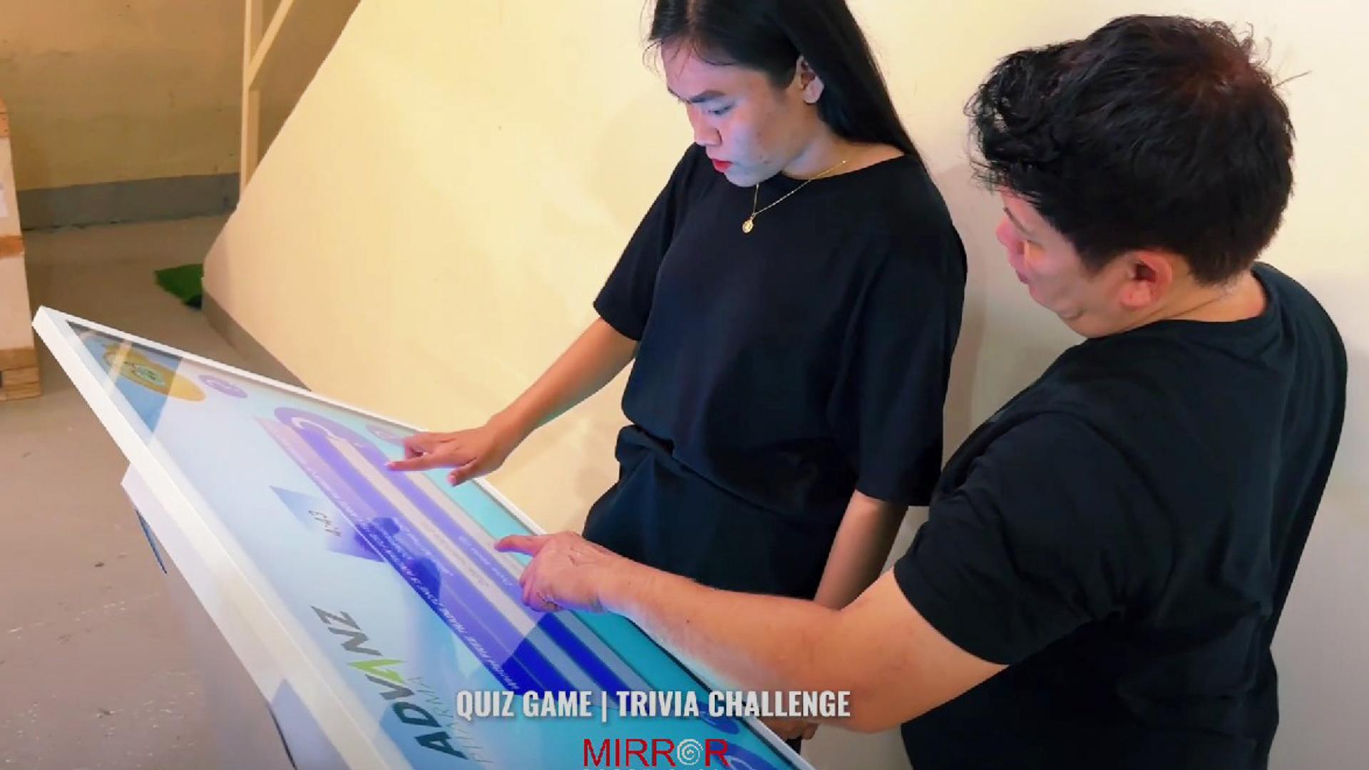 Touchscreen showing quiz results and a Dubai tower trivia question, with answer options and a person in a dark shirt standing beside the screen