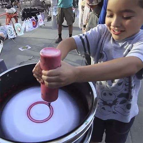 Guest pedaling the Spin Art Bike to create colorful artwork at an event, with vibrant paints splashing onto the spinning canvas.