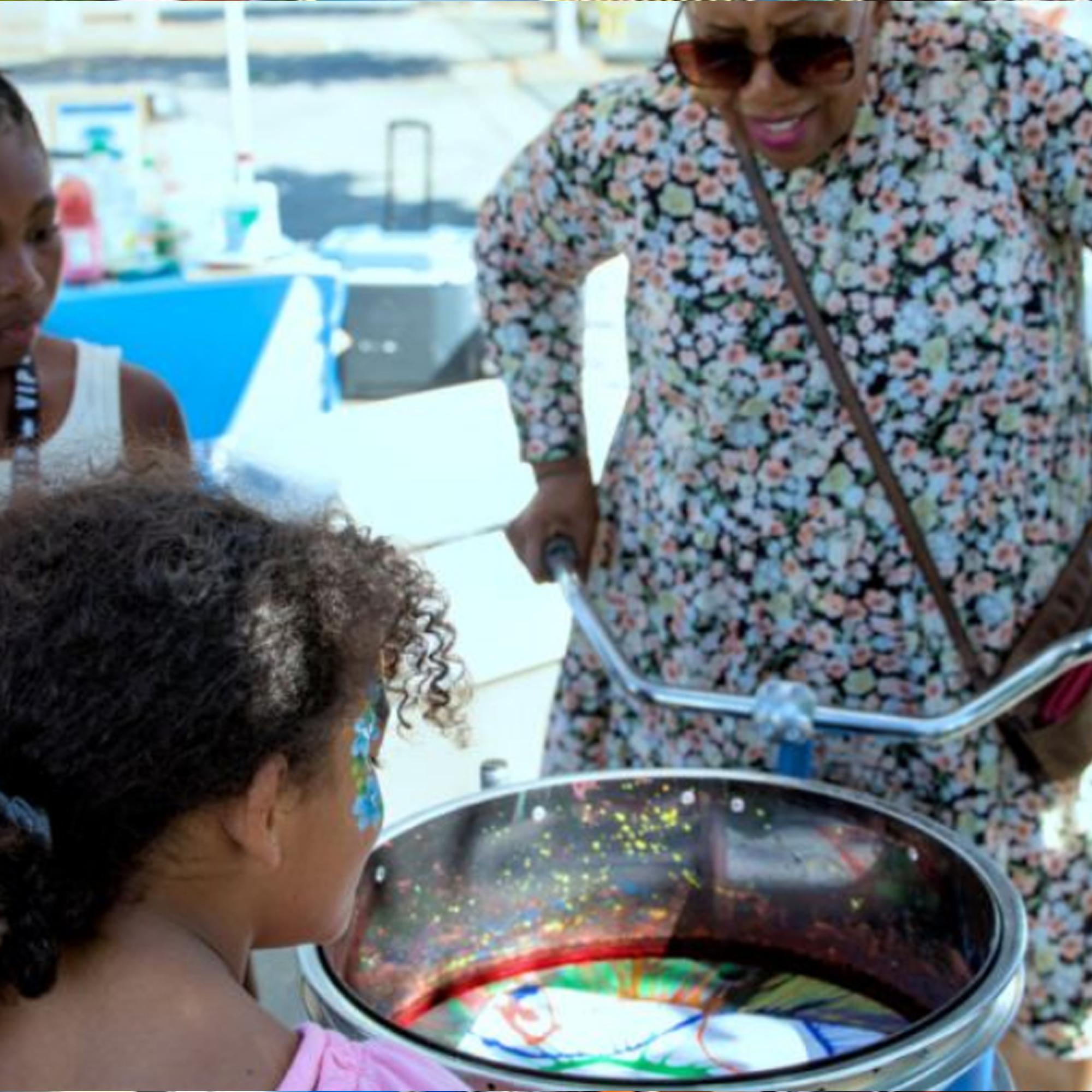 Guest pedaling the Spin Art Bike to create colorful artwork at an event, with vibrant paints splashing onto the spinning canvas.