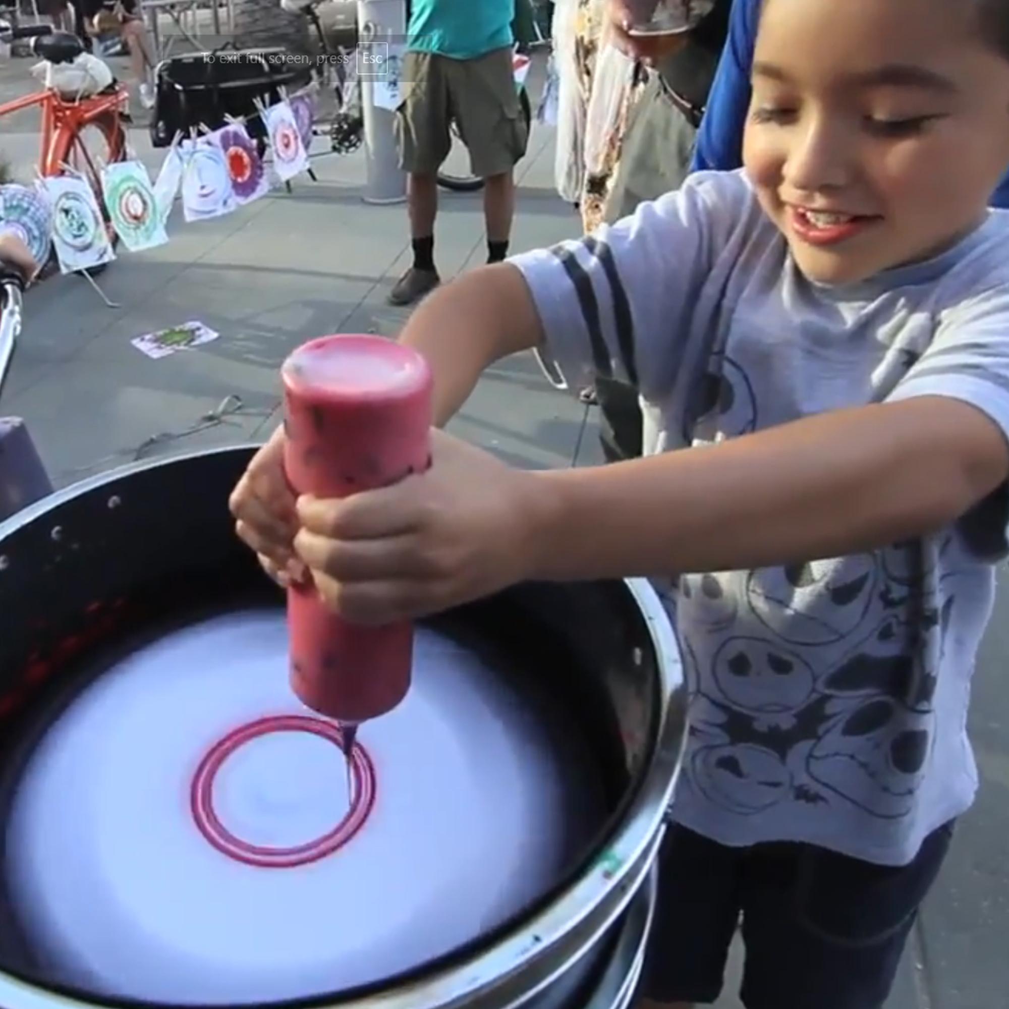 Guest pedaling the Spin Art Bike to create colorful artwork at an event, with vibrant paints splashing onto the spinning canvas.