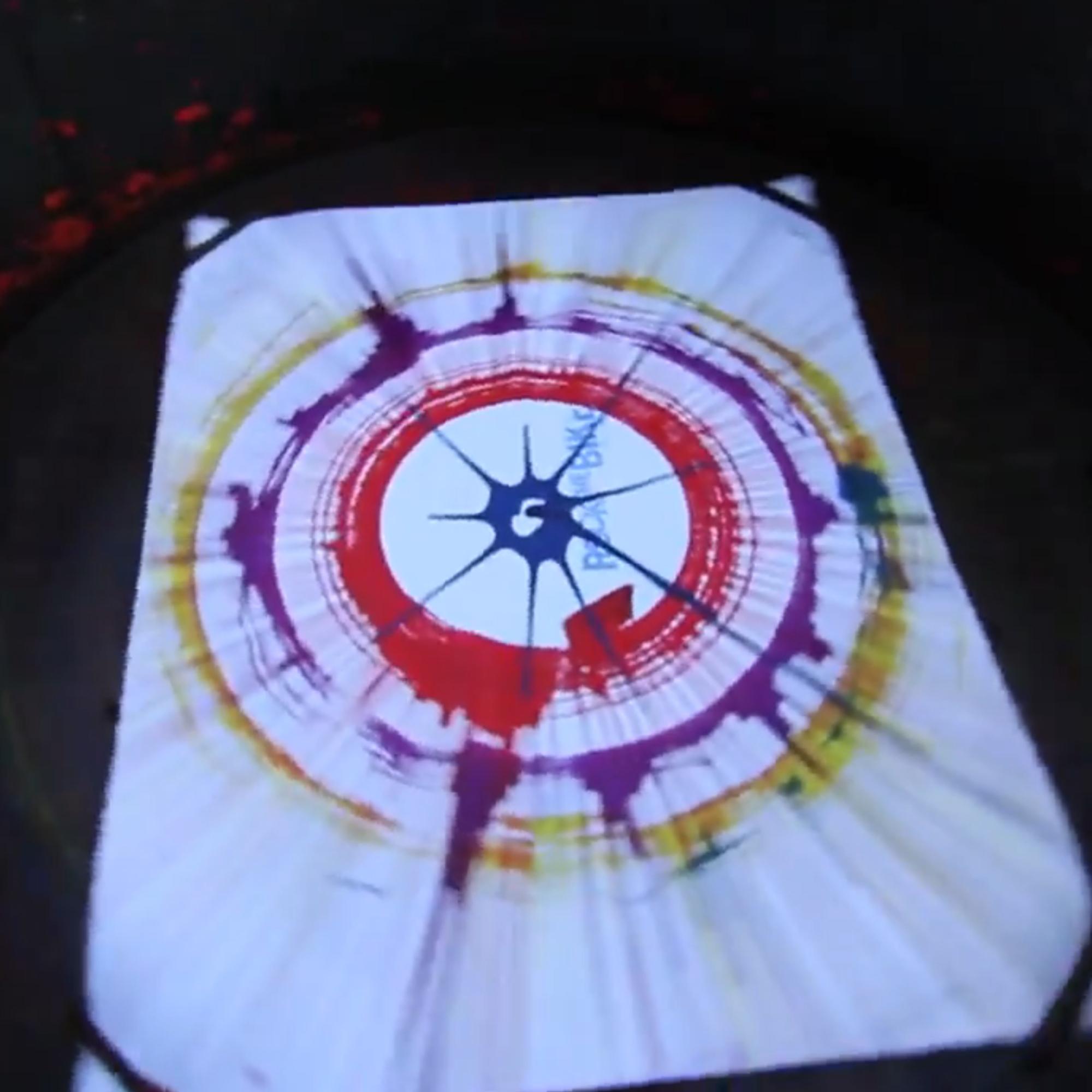 Guest pedaling the Spin Art Bike to create colorful artwork at an event, with vibrant paints splashing onto the spinning canvas.