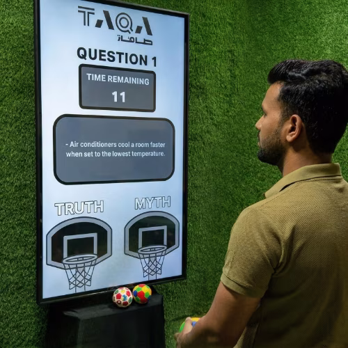 A guest throwing a softball at a large digital Truth or Myth display screen to lock in an answer at a high-energy corporate exhibition booth activation