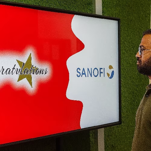 Guest playing word scramble game on large touchscreen at Dubai event with branded graphics and green artificial grass wall background.